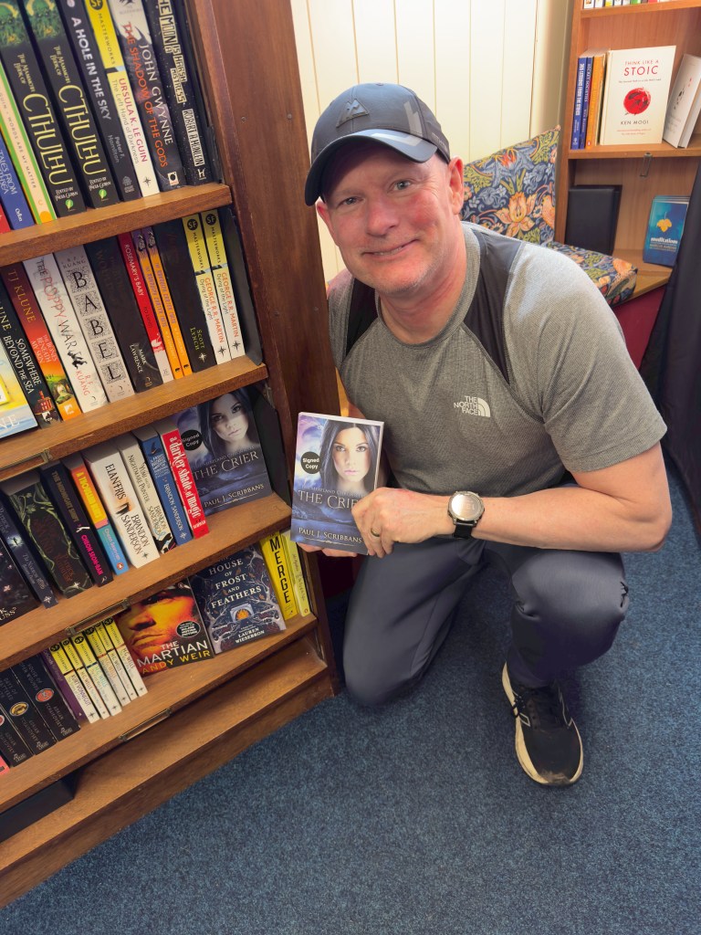 Author holding his book in a bookshop with copies on the shelf behind him