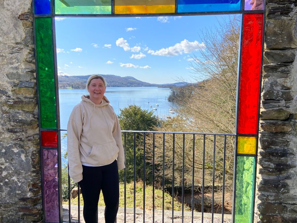 Mrs Scribbans standing inside the stained-glass viewing station at Claife Heights, overlooking Windermere on a sunny day in the Lake District.