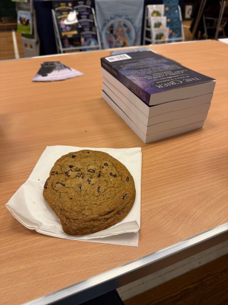 Chocolate chip biscuit beside copies of The Mereland Chronicles: The Crier at the Grasmere Indie Book Fair.