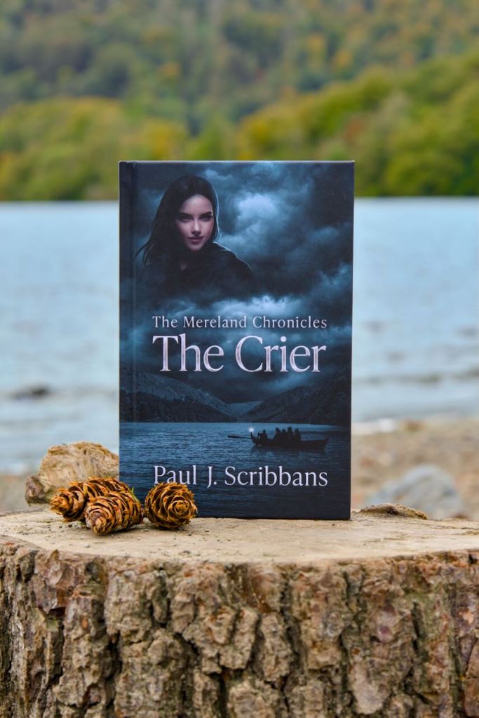 Hardback edition of The Mereland Chronicles: The Crier by P. J. Scribbans displayed on a tree stump beside a lake, with pine cones and woodland in the background.
